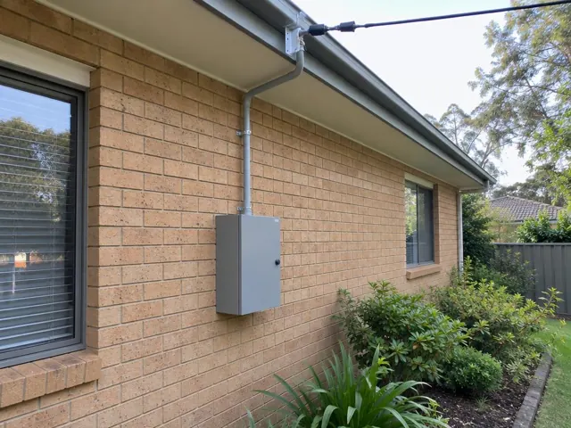 Brick house exterior with new overhead service cable and point-of-attachment bracket near a meter box in Baulkham Hills