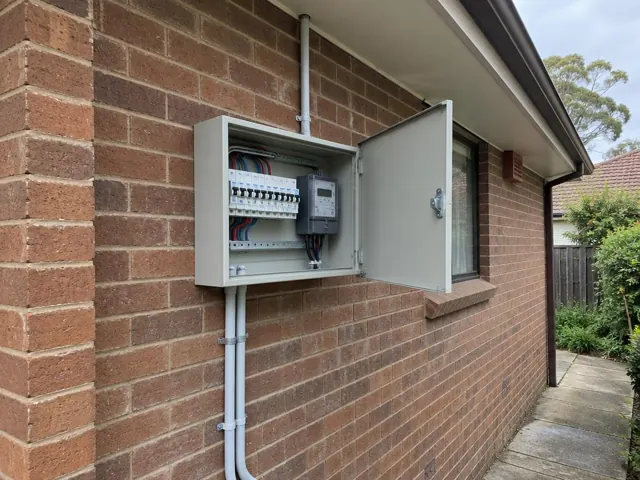 Open external switchboard on a brick house wall beside a window in Thornleigh